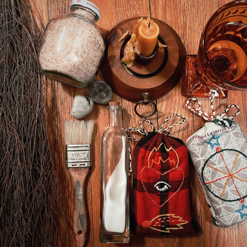 Photo: cinnamon broom, jars of salt, candle, water glass, paint brush, sea stones, and tarot decks